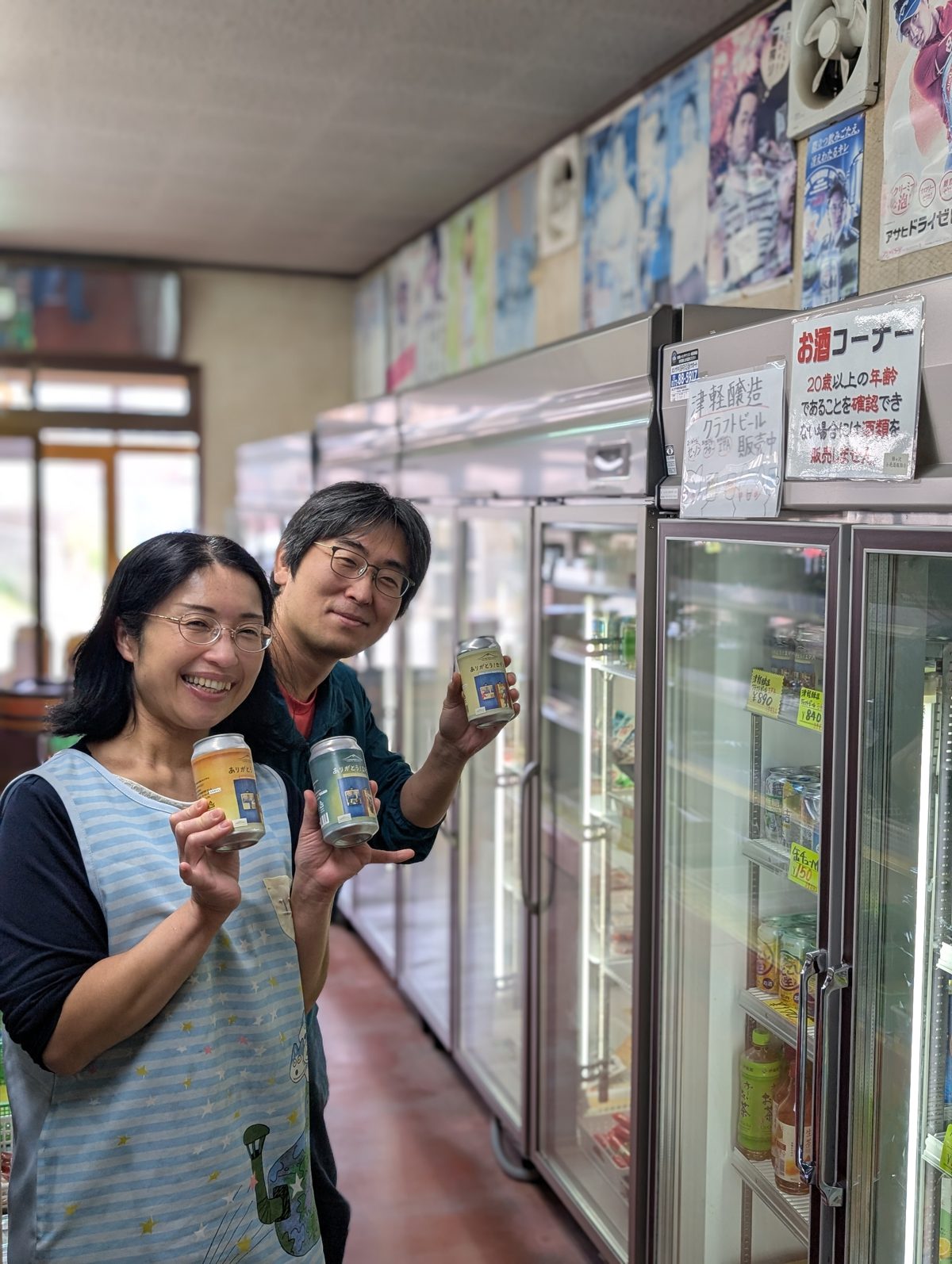 蝦徳商店の店内で、津軽醸造のビールを手に笑顔のお店の方